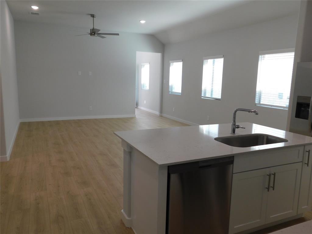 Kitchen featuring a central island with a stone-composite countertop, stainless steel sink, and white cabinetry, complemented by wood-finish flooring, vaulted ceilings, and recessed lighting