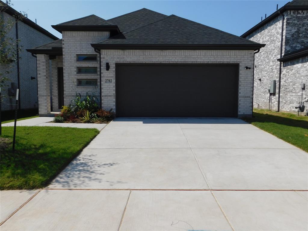Light-toned brick exterior featuring a multi-gabled roofline, concrete driveway, and triple-stacked horizontal windows