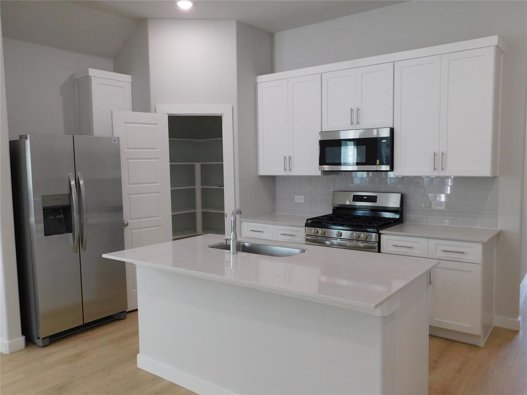 Kitchen featuring white shaker cabinetry, quartz countertops, a central island with an integrated stainless steel sink, stainless steel appliances, and wood-finish flooring