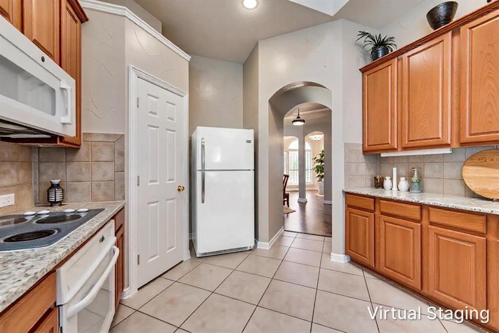 Kitchen featuring wood cabinetry, stone-finish countertops, ceramic tile backsplash, built-in microwave, and arched entryway