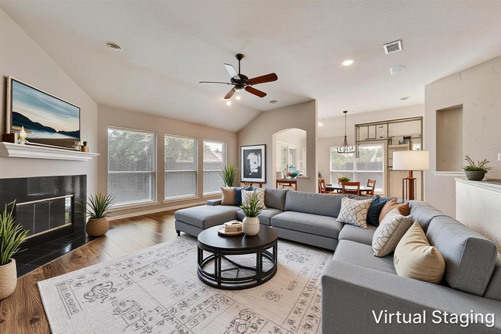 Living area with vaulted ceilings, wood-finish flooring, fireplace with a tiled surround, crown-molded mantel, and a ceiling fan