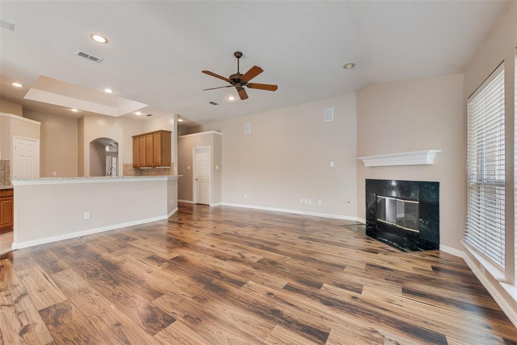 Open living area featuring wood-finish flooring, high ceilings with a central ceiling fan, a corner fireplace with a stone-surround and mantle, and a breakfast bar with stone-finish countertops