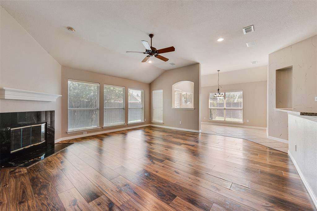 Living area featuring vaulted ceilings, wood-finish flooring, a fireplace with a dark stone surround, a ceiling fan, and large windows