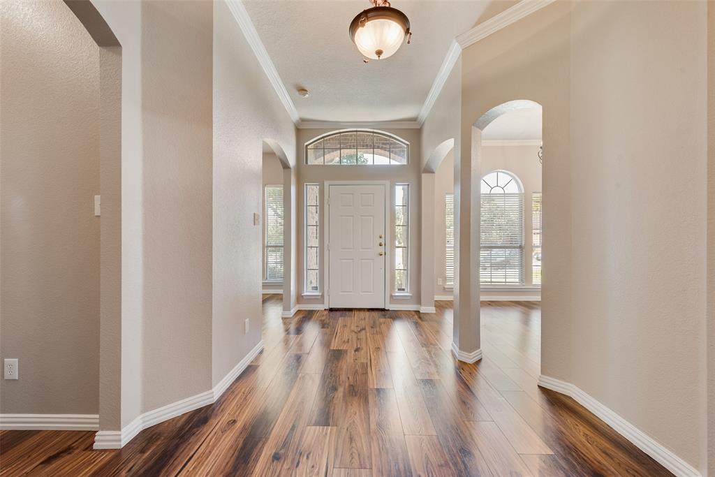Foyer featuring wood-finish flooring, arched entryways, multi-pane transom window, and a semi-flush mount light fixture