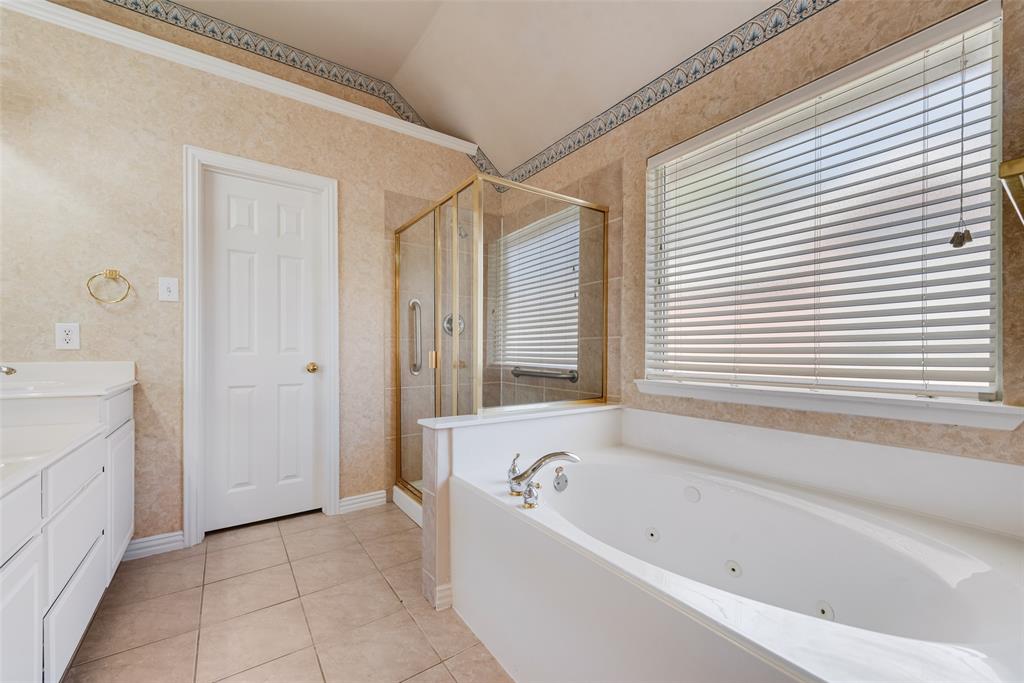 Bathroom featuring a jetted soaking tub, glass-enclosed shower with gold-tone hardware, tile flooring, and vaulted ceiling