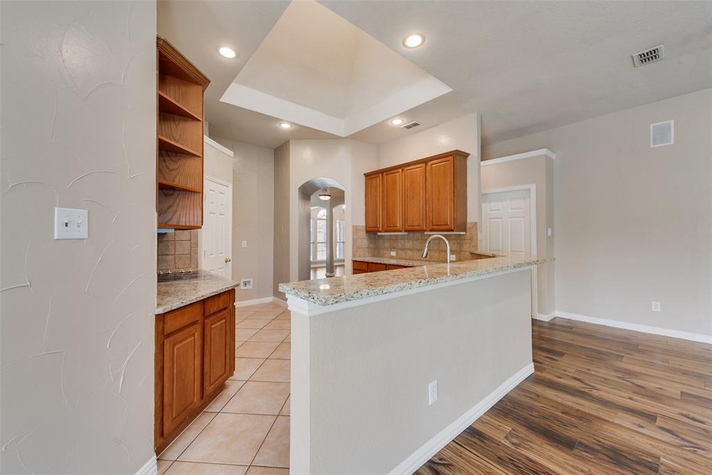 Kitchen featuring a raised tray ceiling, wood-finish cabinetry, natural stone countertops, recessed lighting, and tile flooring