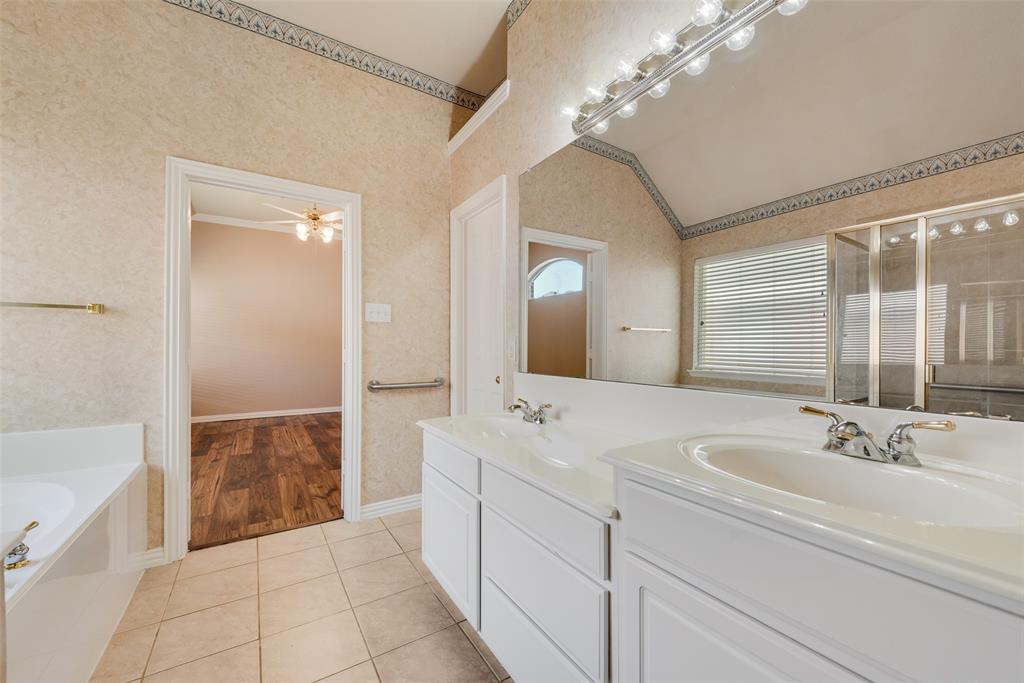 Bathroom featuring a dual-sink vanity with white cabinetry, a full-width mirror, tile flooring, and a separate bathtub and glass-enclosed shower
