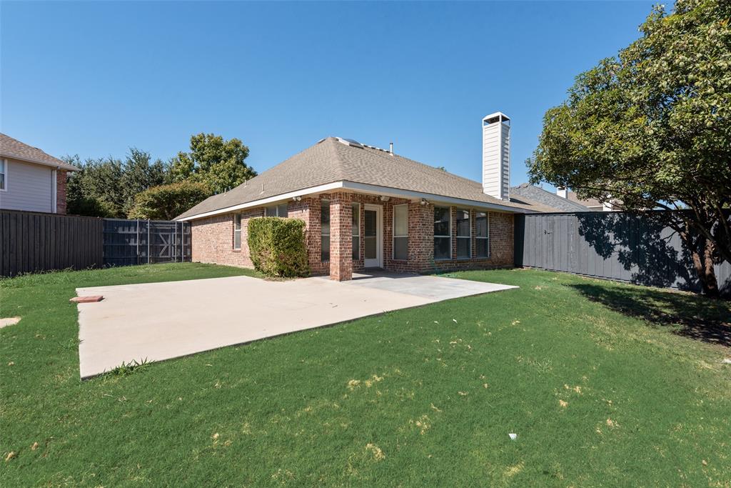 Exterior rear elevation featuring a brick facade, chimney, concrete patio, and fenced perimeter
