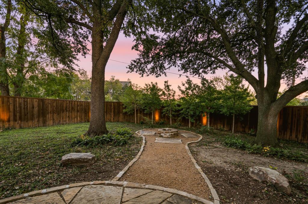Backyard featuring a stone-lined gravel path, stone fire pit, wood privacy fencing, and mature trees