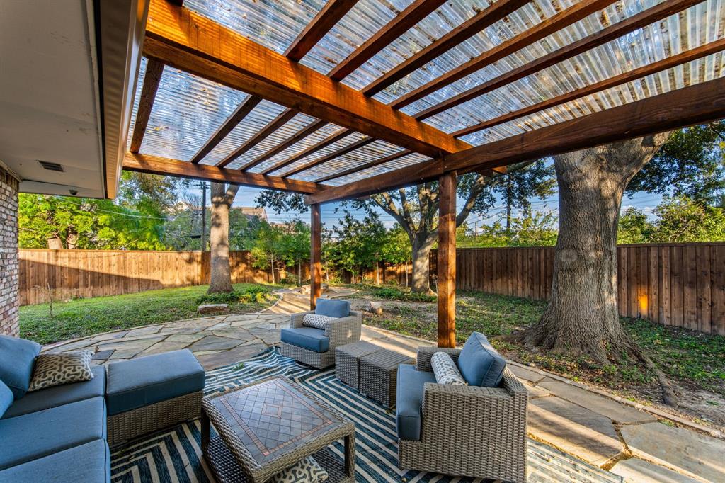 Covered patio featuring a timber-frame pergola with a translucent corrugated roof, flagstone hardscaping, and a perimeter wood privacy fence