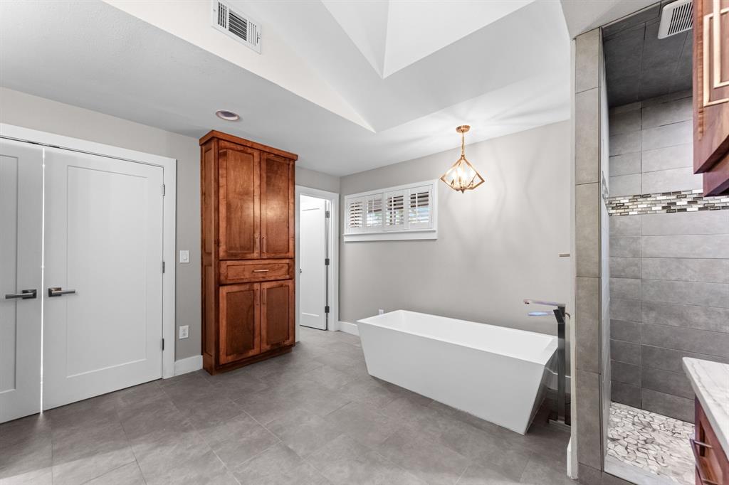 Vaulted ceiling featuring a built-in wood cabinet, freestanding soaking tub and a tiled shower with stone-style flooring