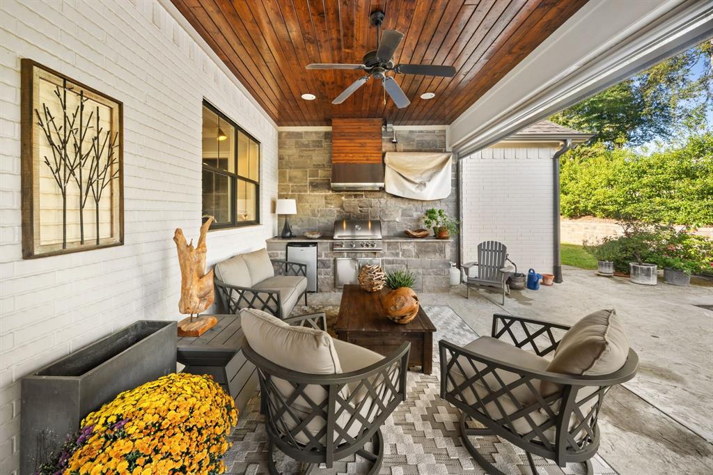 Covered patio featuring a stained wood plank ceiling, stone masonry wall, built-in outdoor kitchen with a stainless steel grill, and integrated recessed lighting Covered patio featuring a stained wood plank ceiling, stone masonry wall, built-in outdoor kitchen with a stainless steel grill, and integrated recessed lighting