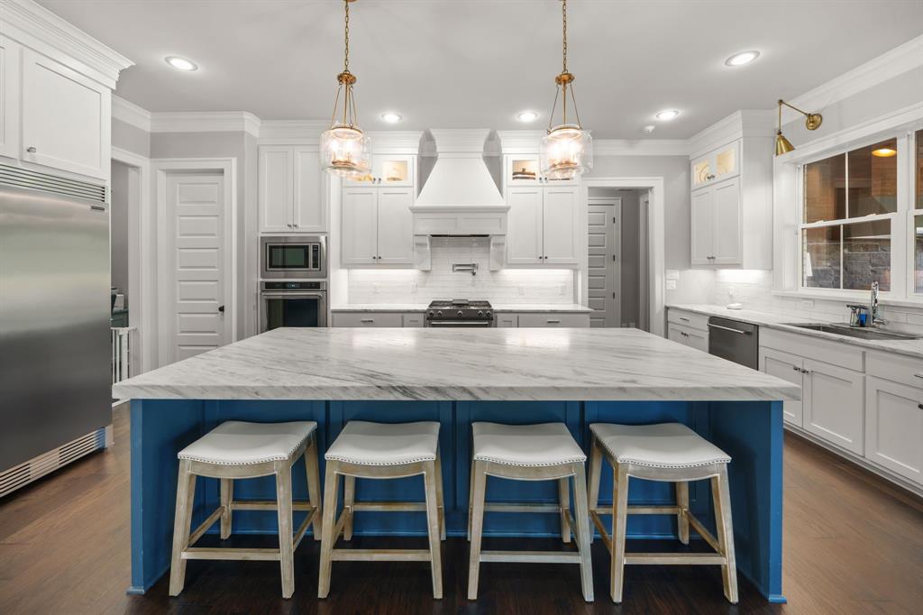 Kitchen featuring a large central island with a stone countertop, white cabinetry with crown molding, stainless steel built-in appliances, recessed lighting, and wood-finish flooring