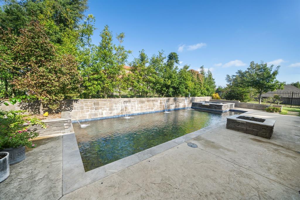 Rectangular swimming pool with integrated water features and a stone-clad retaining wall, accompanied by a raised spa, stone fire feature, and concrete patio
