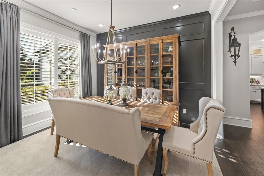 Dining room featuring dark wood-finish flooring, custom-paneled accent wall, plantation shutters, recessed lighting, and a multi-tiered chandelier