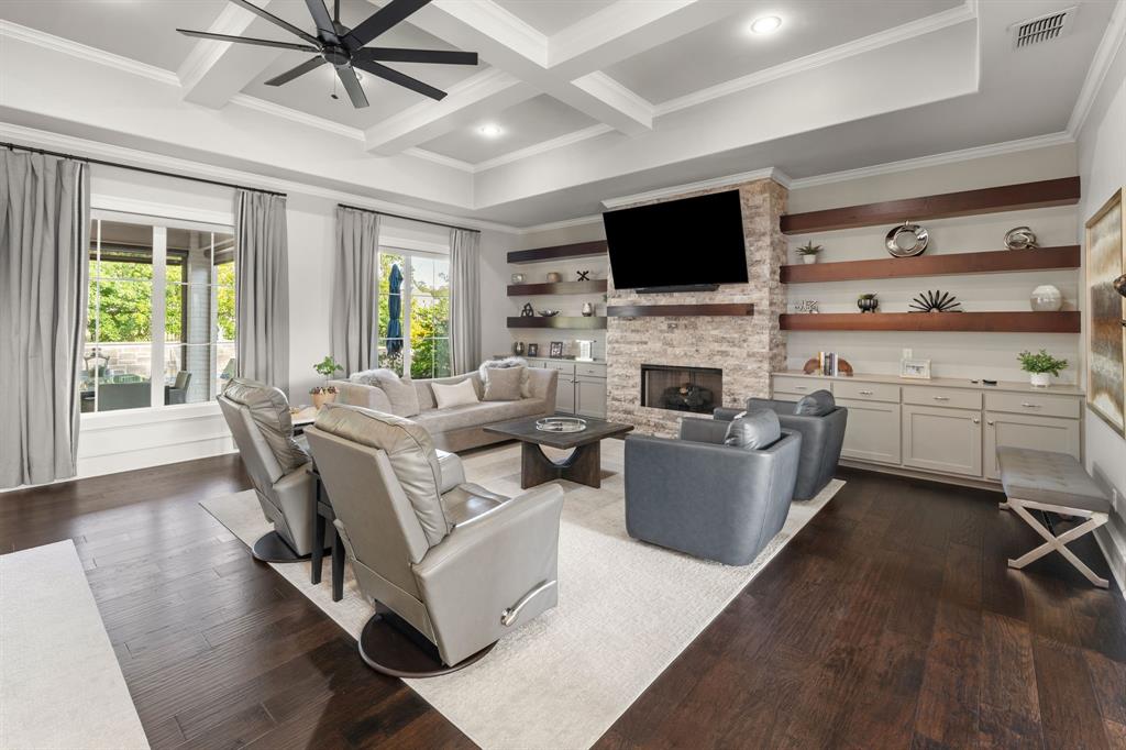 Living area featuring wood-finish flooring, coffered ceiling, stone-surround fireplace, and built-in cabinetry with floating wood shelving