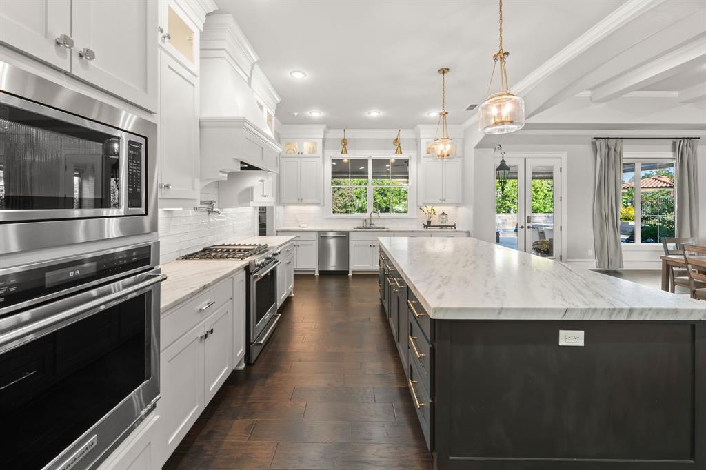Gourmet kitchen featuring a large central island with stone-finish countertops, custom cabinetry with brushed gold hardware, stainless steel appliances, and dark wood-finish flooring