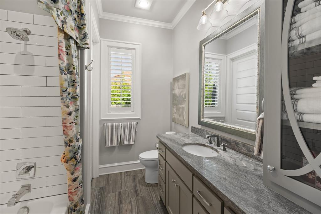 Bathroom featuring a stone-surface vanity with an integrated sink, white subway tile shower surround, interior window shutters, and built-in cabinetry with decorative glass inlay