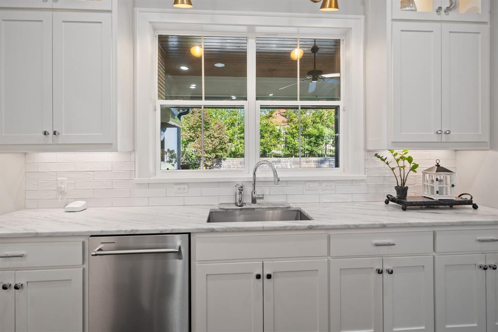 Kitchen featuring white Shaker-style cabinetry, stone-patterned countertops, a white subway tile backsplash, stainless steel under-mount sink with a gooseneck faucet, and an integrated stainless steel dishwasher