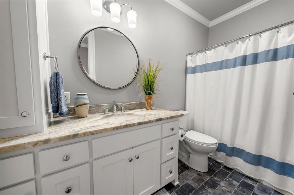 Bathroom featuring a white shaker-style vanity with stone-patterned countertop, integrated basin, round mirror, and tile flooring
