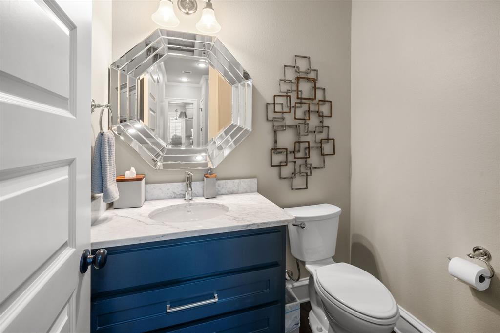 Navy blue vanity with stone countertop, integrated sink, and chrome fixtures, paired with a multi-faceted octagonal mirror and dual-light wall sconce