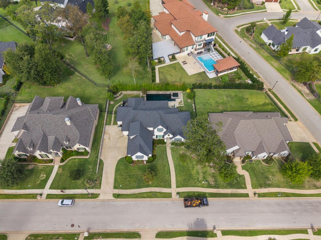 Aerial perspective of a multi-gabled residence featuring a dark shingle roof, concrete driveway, stone-accented exterior, and a private rear swimming pool