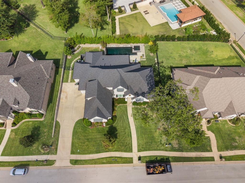 Aerial perspective featuring a multi-gabled roofline, concrete driveway, stone-paved walkway, and a rectangular swimming pool with an integrated spa