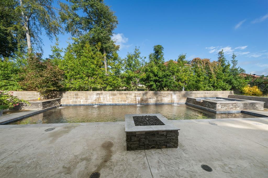 Swimming pool with stone-veneer retaining wall and integrated water features, raised stone-clad spa, and square stone-top fire pit set within a stamped concrete deck