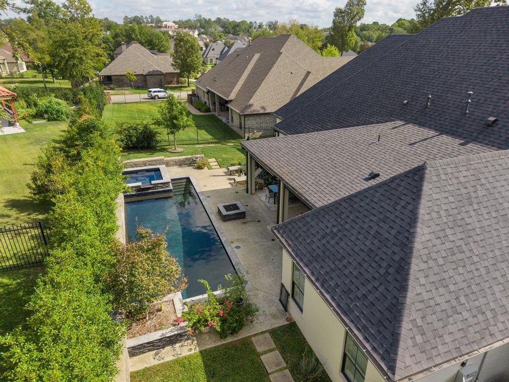 Exterior backyard featuring a rectangular swimming pool, raised spa with stone veneer, covered patio, integrated fire pit, and professional landscaping