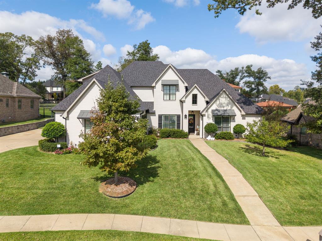 Two-story brick exterior featuring a multi-gabled roofline, architectural asphalt shingles, dark metal window awnings, and a manicured lawn with mature landscaping