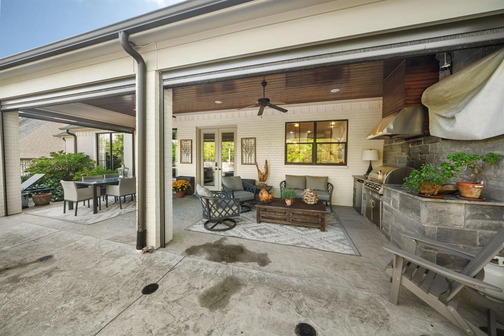 Covered patio featuring a wood-plank ceiling, ceiling fan, built-in outdoor kitchen with a stainless steel vent hood, stone-veneer cooking station, and painted brick exterior walls Covered patio featuring a wood-plank ceiling, ceiling fan, built-in outdoor kitchen with a stainless steel vent hood, stone-veneer cooking station, and painted brick exterior walls