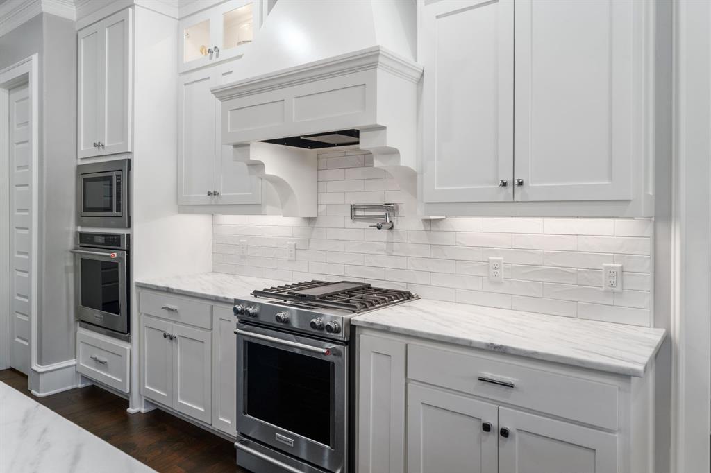 Kitchen featuring white shaker-style cabinetry, natural stone countertops, subway tile backsplash, stainless steel gas range with a custom decorative vent hood, and built-in wall oven and microwave