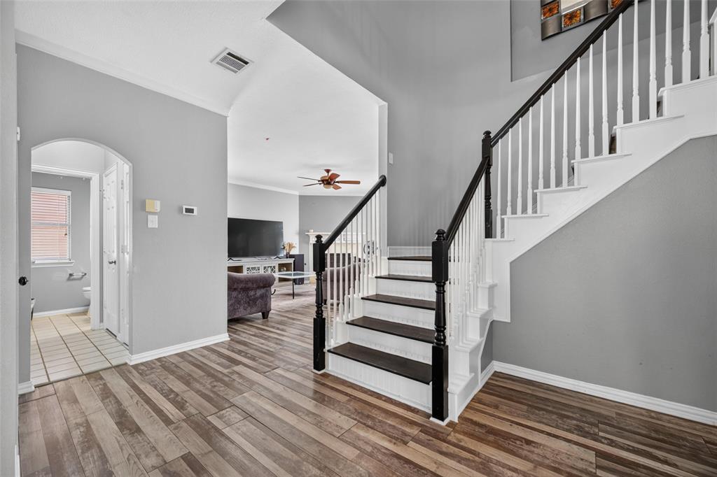 Entryway featuring wood-finish flooring, vaulted ceilings, and a staircase with white balusters and dark wood-finish treads
