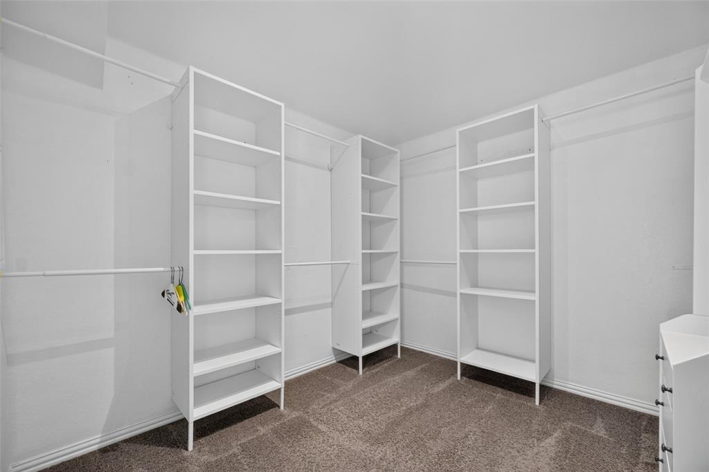 Walk-in closet featuring white built-in shelving units, multiple hanging rods, and neutral carpeting