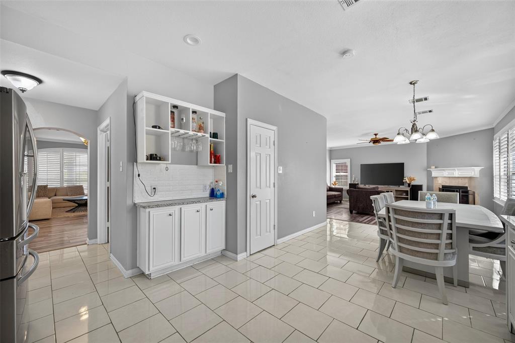 Built-in wet bar featuring white cabinetry, subway tile backsplash, and stone countertop, complemented by large-format tile flooring and recessed lighting