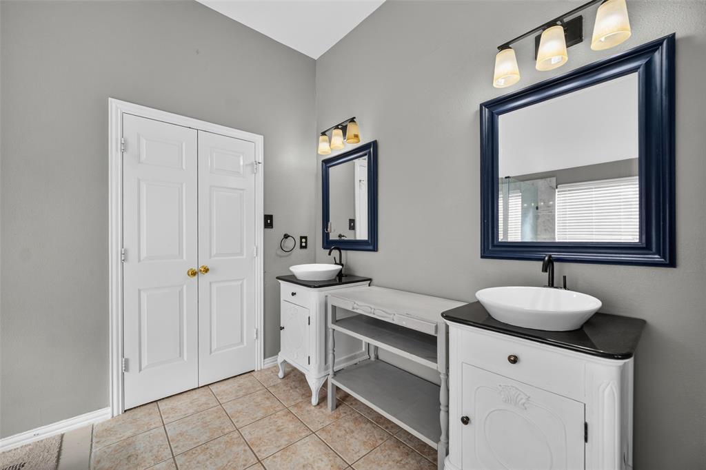 Dual vanities featuring white cabinetry, dark stone-finish countertops, ceramic vessel sinks, and dark metal faucets, accented by wall-mounted lighting and matching framed mirrors