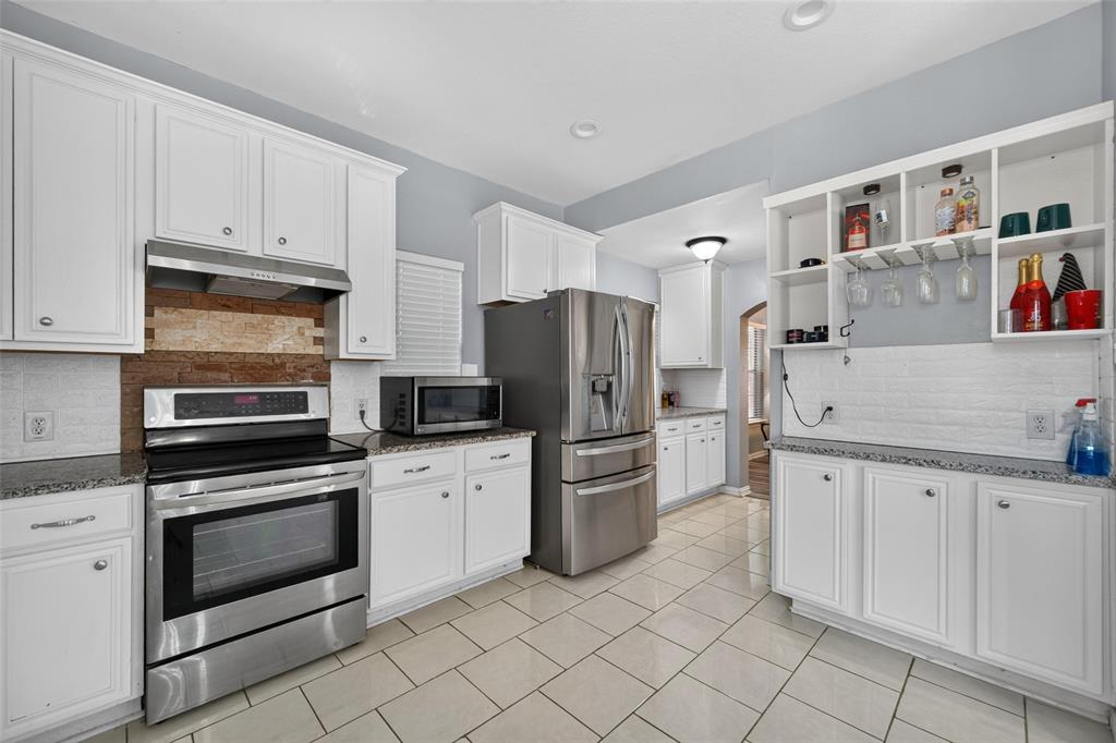 Kitchen featuring white shaker-style cabinetry, stainless steel appliances, speckled stone-finish countertops, textured brick-style backsplash, and ceramic tile flooring