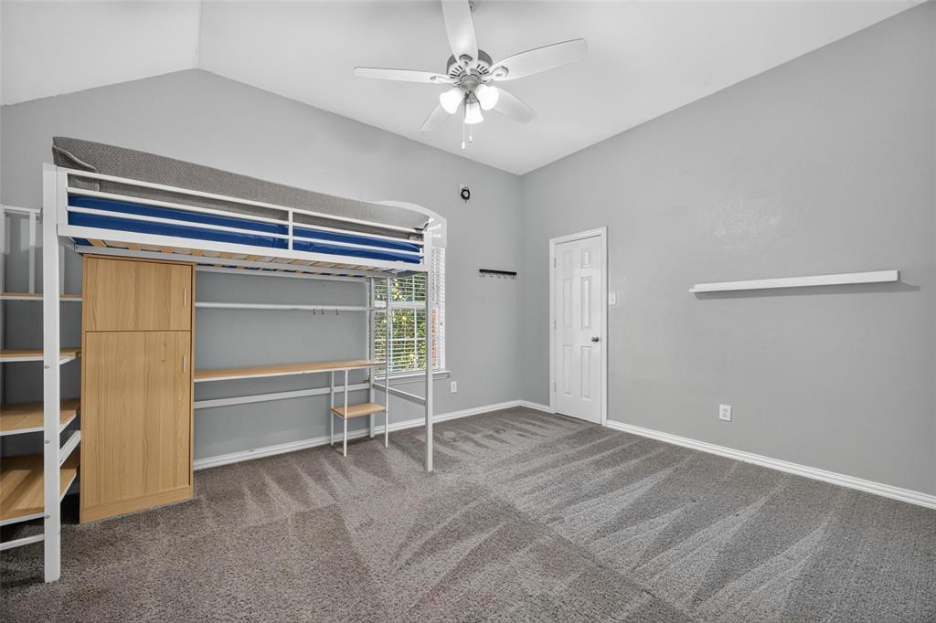 Vaulted ceilings, neutral carpeting, a ceiling fan with integrated lighting, and a wall-mounted floating shelf