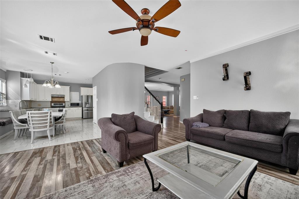 Open-concept interior featuring wood-finish flooring, a ceiling fan with integrated lighting, neutral wall paint, tile flooring in the kitchen area, and a curved architectural wall partition