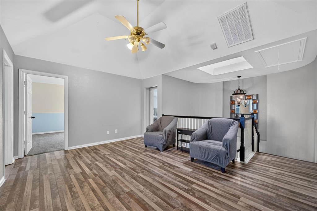 Vaulted ceiling with a centrally mounted ceiling fan, wood-finish flooring, integrated skylight, and a decorative staircase railing with a hanging pendant light