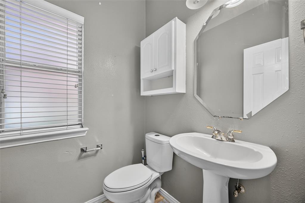 White pedestal sink with polished metal faucet, octagonal wall-mounted mirror, white wall-mounted cabinet, and horizontal window blinds