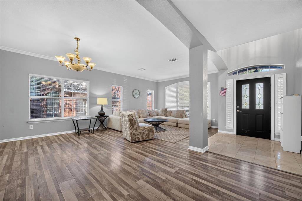 Open-concept interior featuring wood-finish flooring, a neutral color palette, arched architectural detailing, a multi-pane front door with a transom window, and a decorative ceiling-mounted chandelier