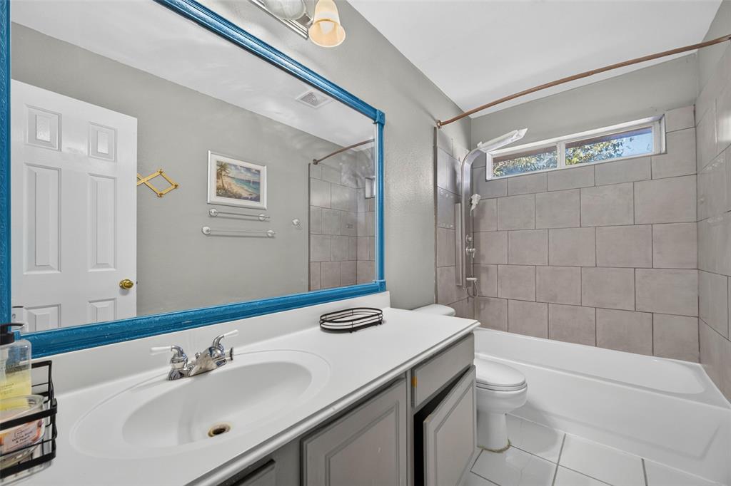 Bathroom featuring a white vanity with a solid-surface countertop, an inset basin, a full-width mirror, tile-surround shower-tub combination, and a transom window