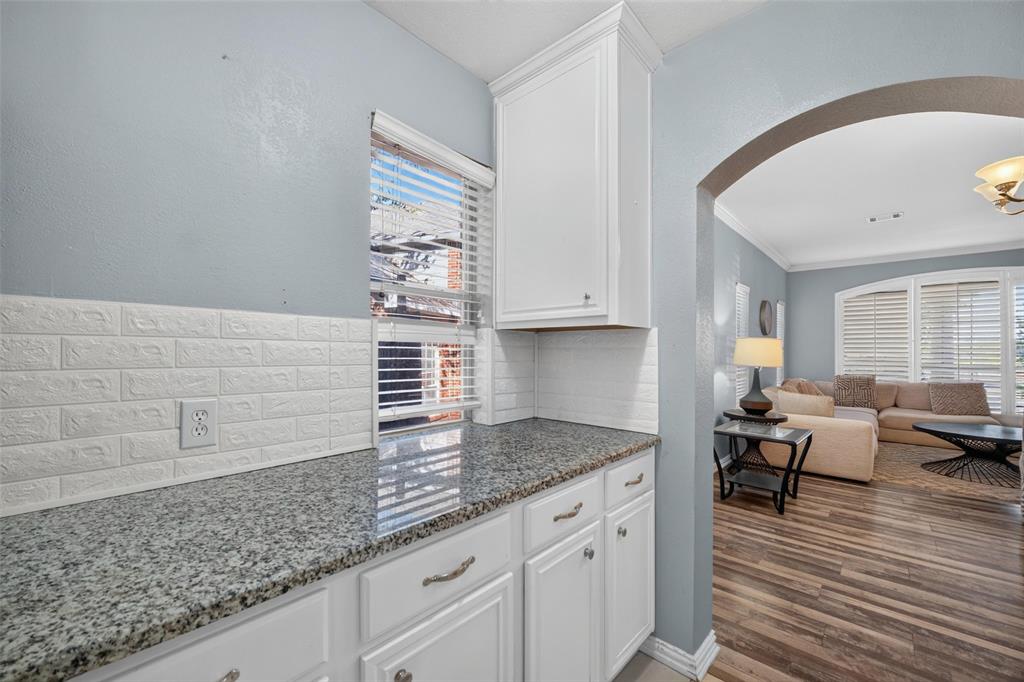 Kitchen featuring stone-finish countertops, white cabinetry, textured tile backsplash, and wood-finish flooring, accented by an architectural archway
