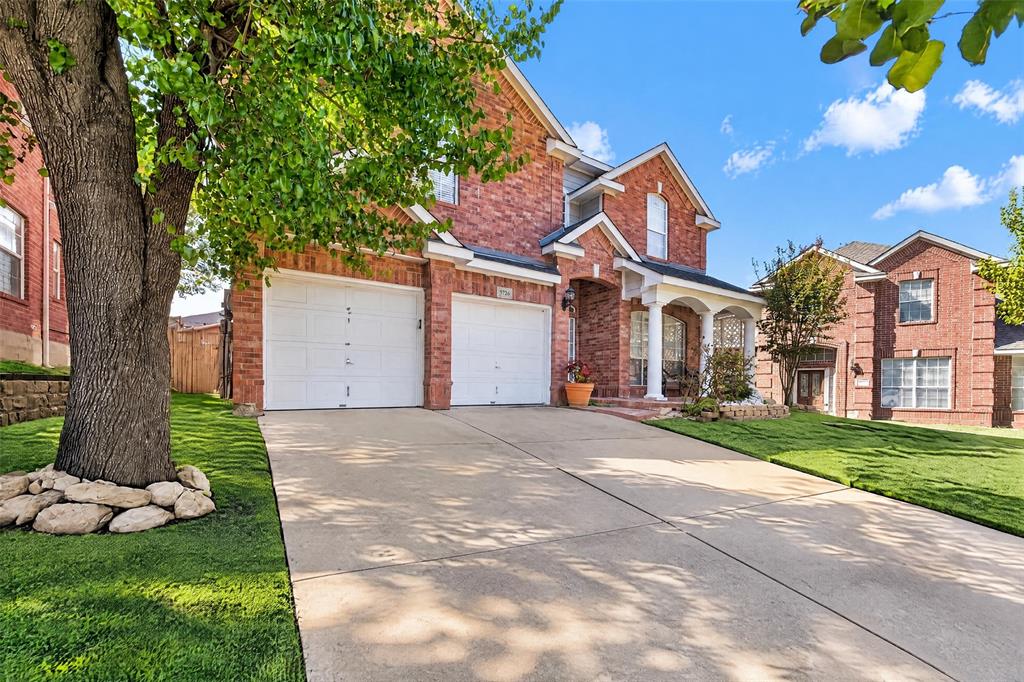 Two-story brick exterior featuring a covered front porch with columns, a two-car garage, and a concrete driveway