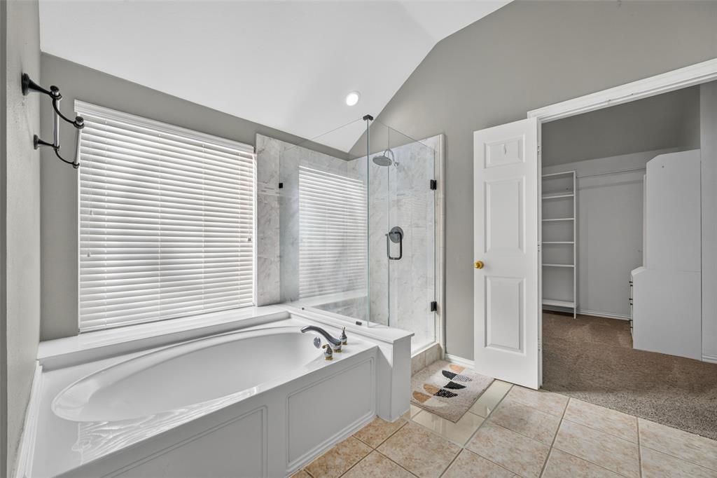Bathroom featuring a vaulted ceiling, soaking tub with a deck mount faucet, walk-in glass-enclosed shower with stone-surround tile, and ceramic tile flooring