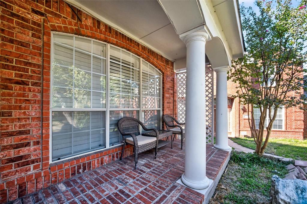 Covered brick porch featuring structural columns, decorative lattice screening, and multi-pane windows with brick trim
