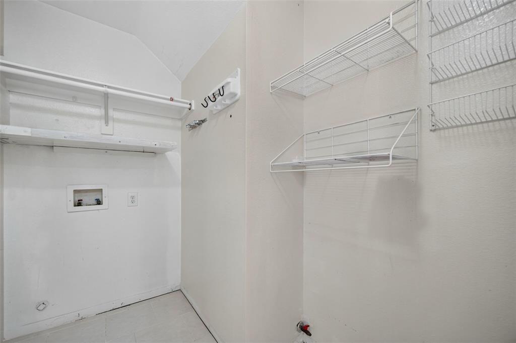 Utility area featuring built-in wire shelving, overhead storage racks, wall-mounted utility hooks, and dedicated water and electrical hookups