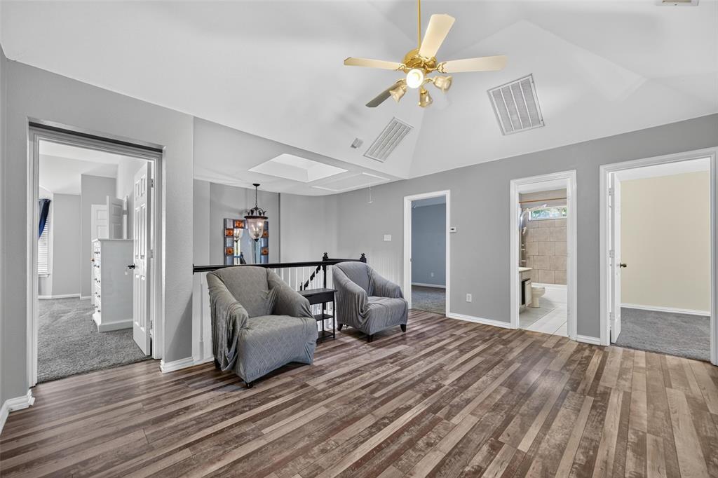 Vaulted ceiling featuring a skylight, wood-finish flooring, and a ceiling-mounted light fixture with a fan