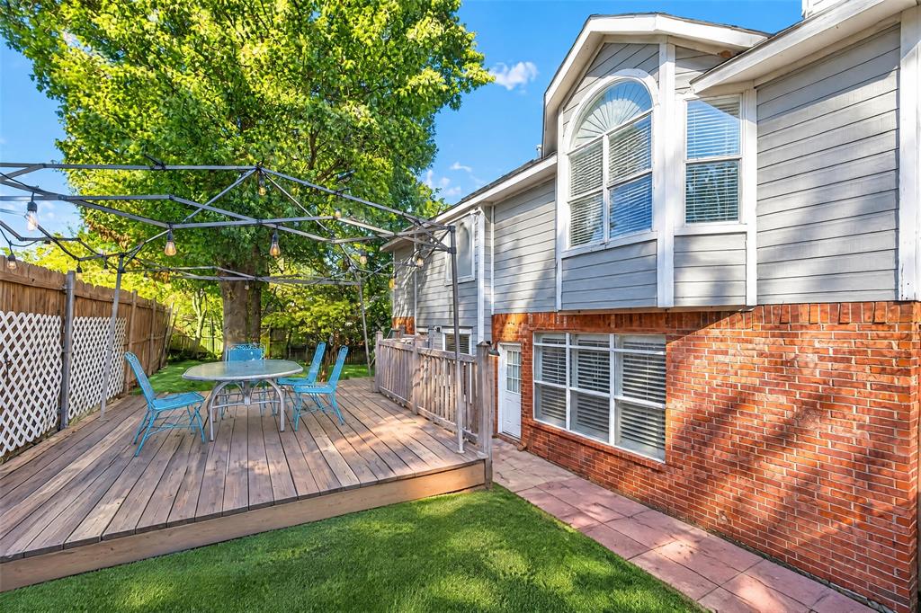 Multi-level exterior featuring a brick and horizontal siding facade, elevated wood deck, metal lattice pergola, and a stone-paver walkway
